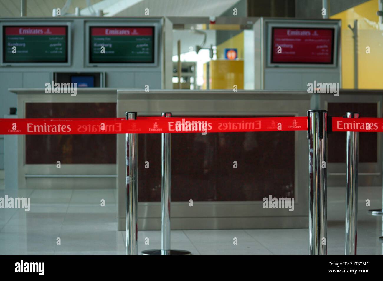 View of red retractable belt barrier and Emirates Airlines logo at departure gate in Dubai International Airport terminal with bokeh background. Stock Photo