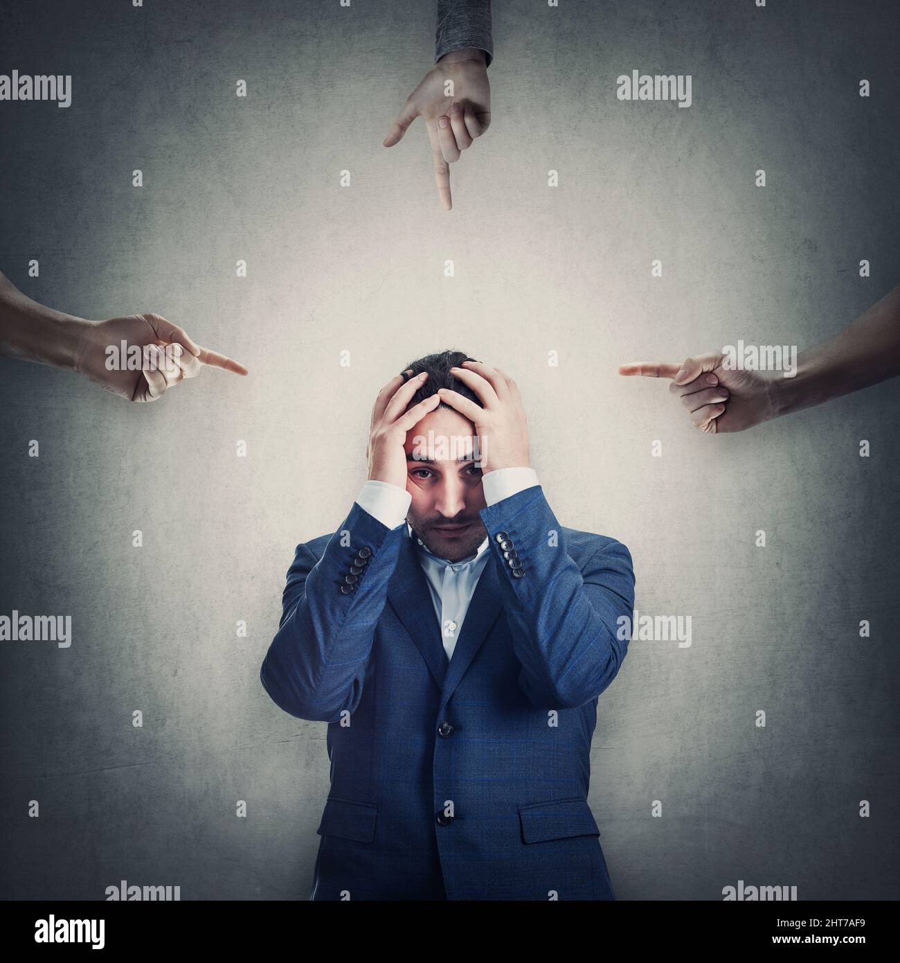 Ashamed and desperate businessman covers head with hands, as multiple persons pointing fingers towards him, blaming and scolding. Man suffering emotio Stock Photo
