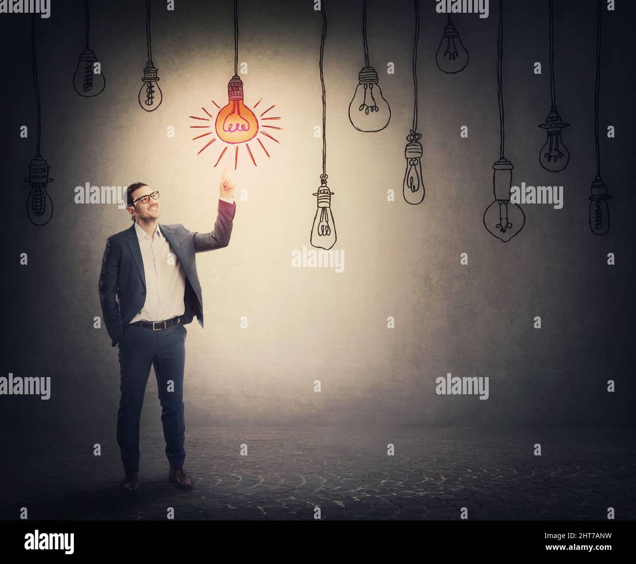 Cheerful businessman points up index finger, showing an enlightened light bulb among multiple others switched off. Business metaphor, idea choice conc Stock Photo