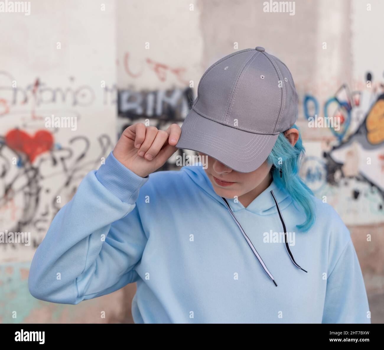 Blue haired Teenage girl in blue hoodie and baseball cap touching her cap. Blue haired teen girl