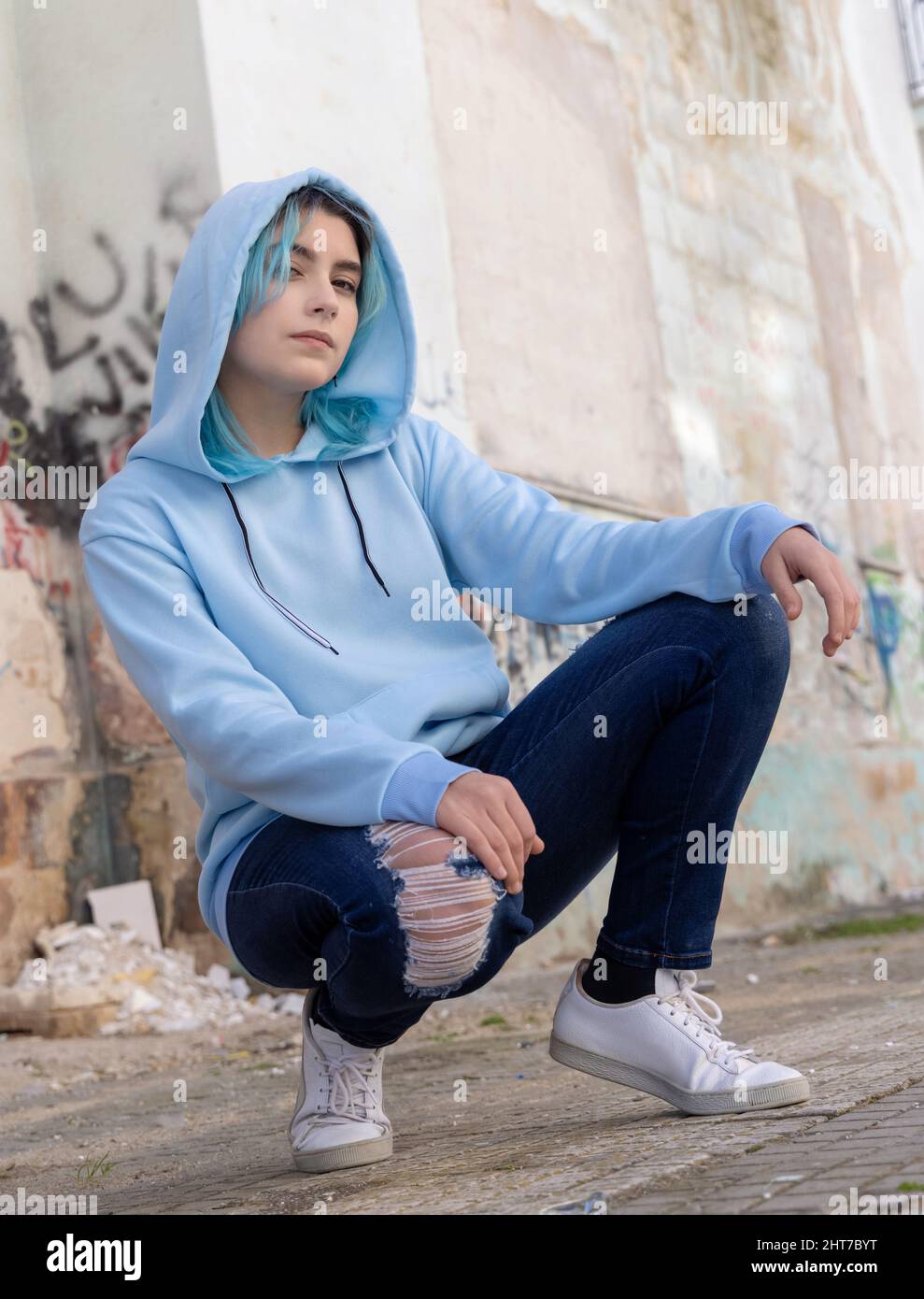 Blue haired Teenage girl in blue hoodie staying near graffiti wall with red water  bottle Stock Photo by katrinshine