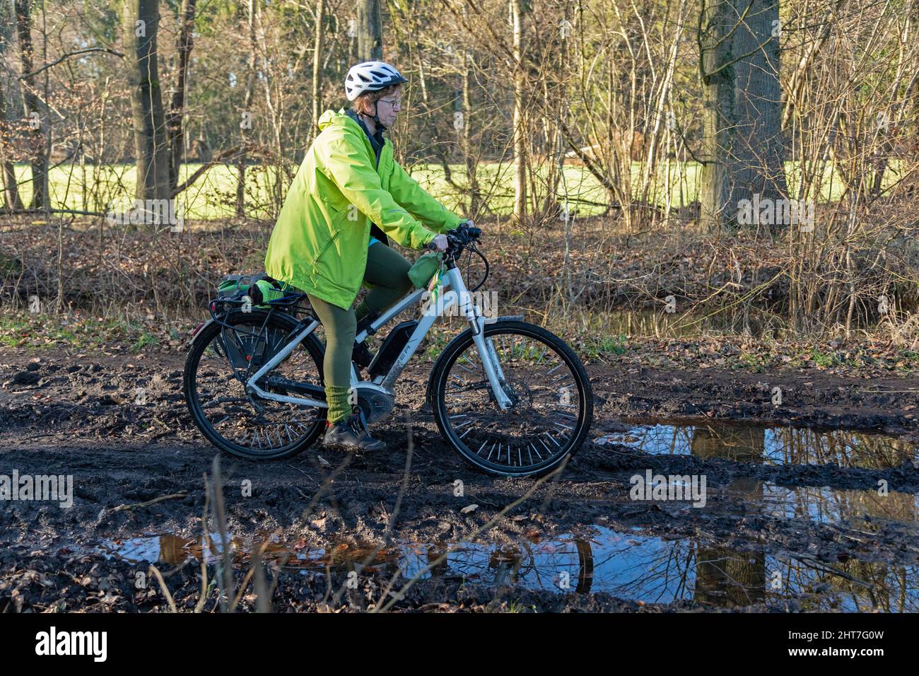 Woman over fifty doing a cycling tour with her e-bike along a muddy path and through puddles, Lueneburg, Lower Saxony, Germany Stock Photo