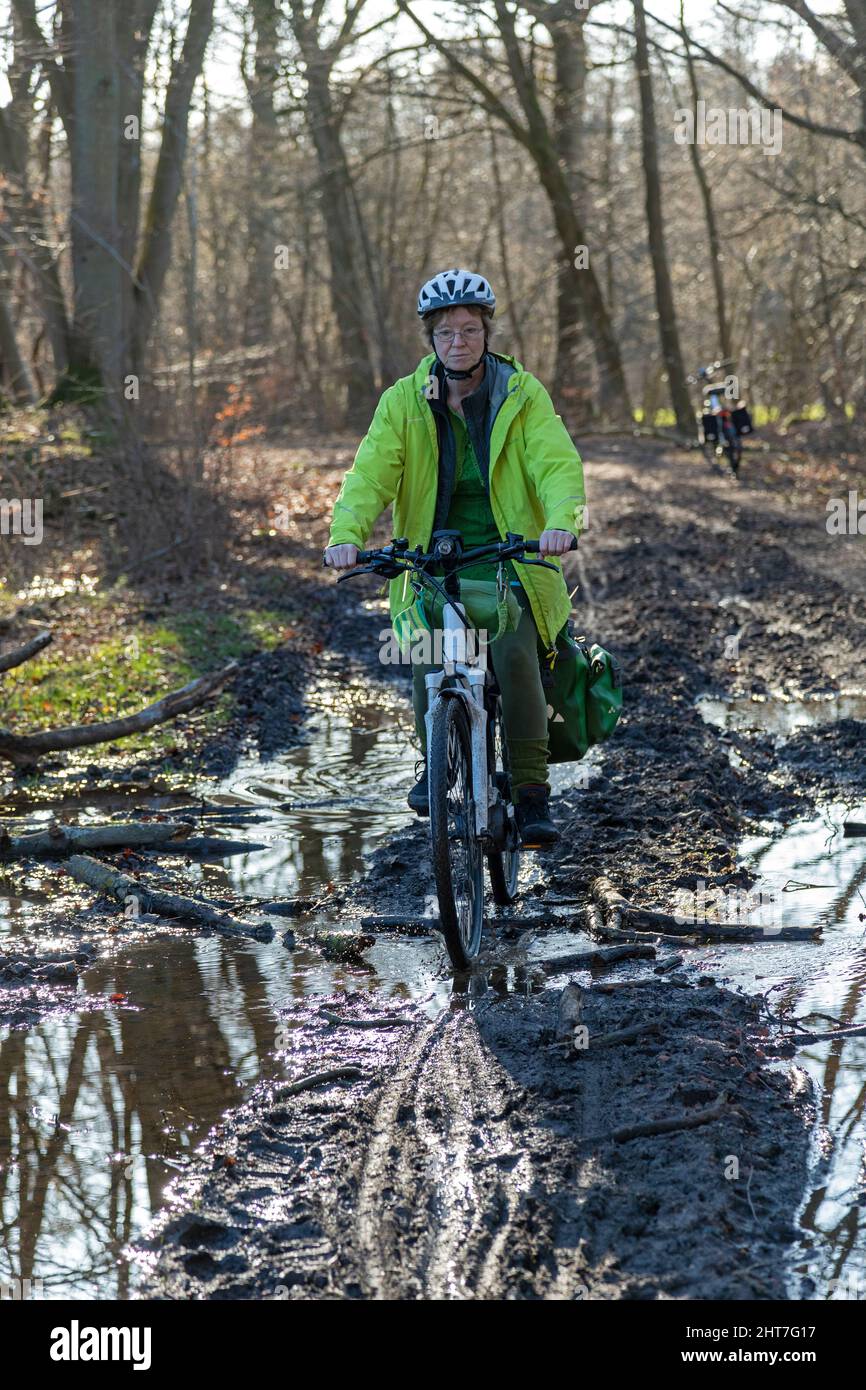 Woman over fifty doing a cycling tour with her e-bike along a muddy path and through puddles, Lueneburg, Lower Saxony, Germany Stock Photo