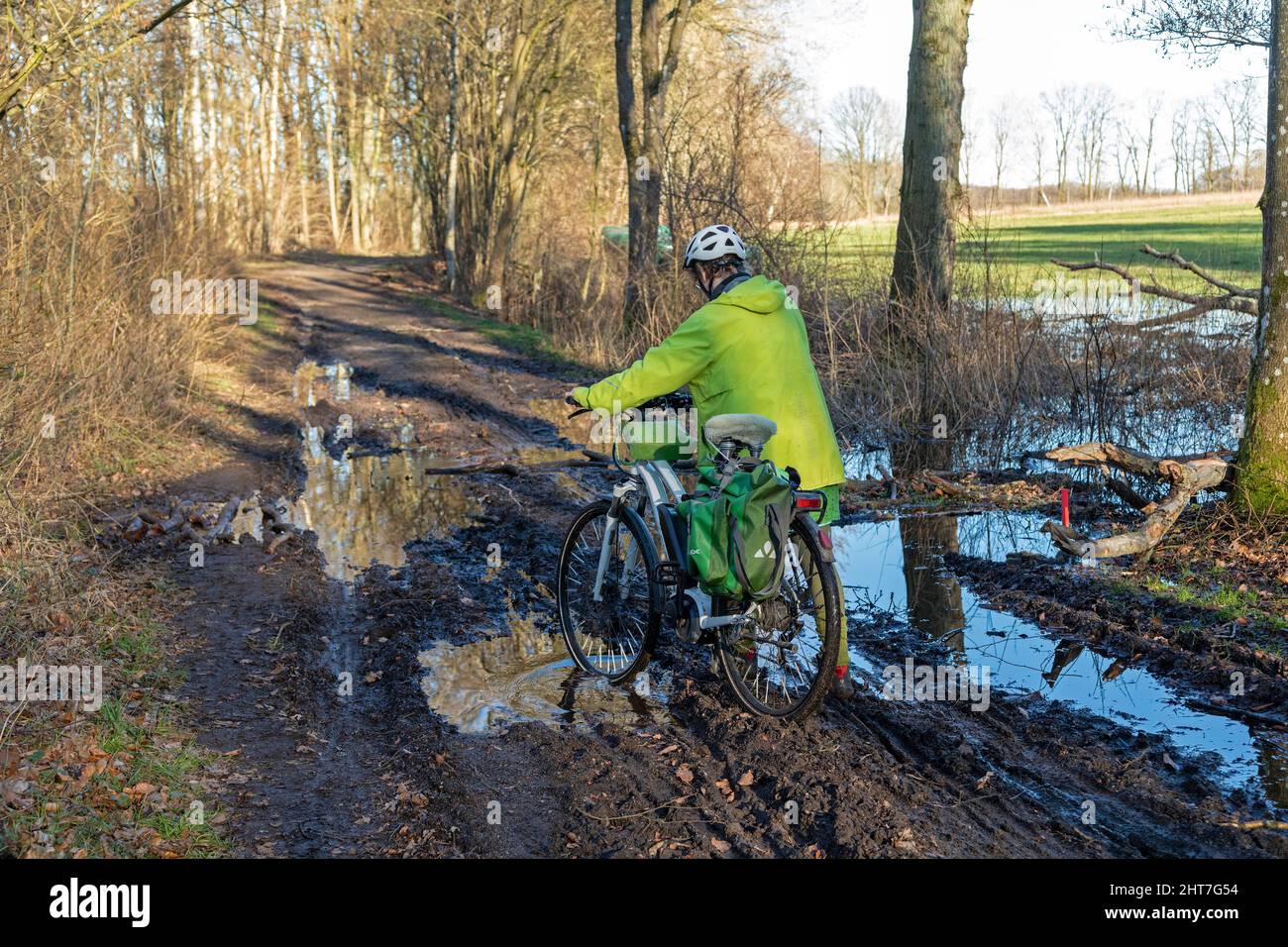 Woman over fifty doing a cycling tour with her e-bike along a muddy path and through puddles, Lueneburg, Lower Saxony, Germany Stock Photo