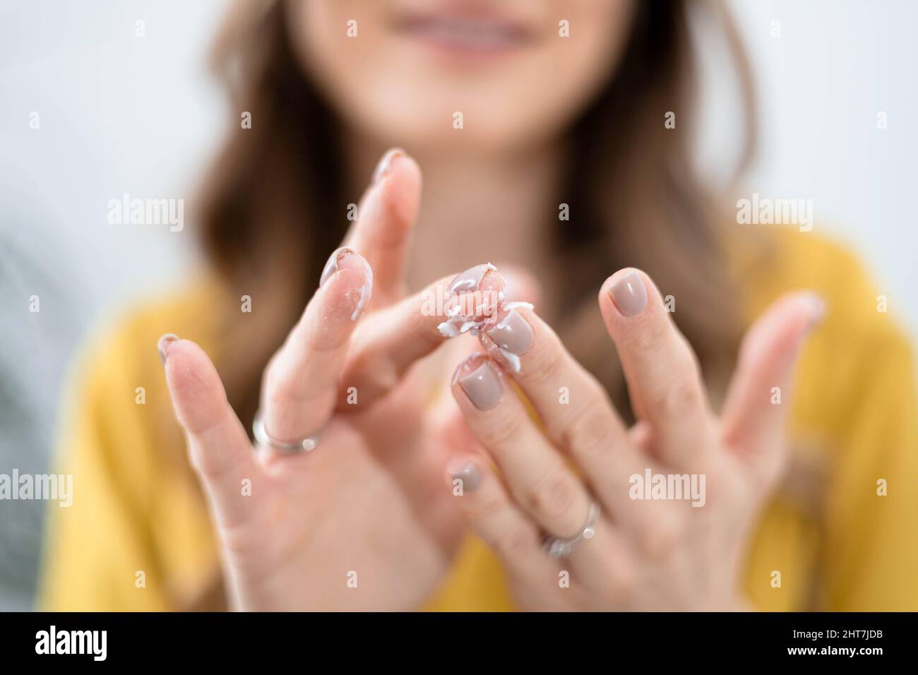 Young brunette woman uses cosmetic cream, close-up on hands Stock Photo