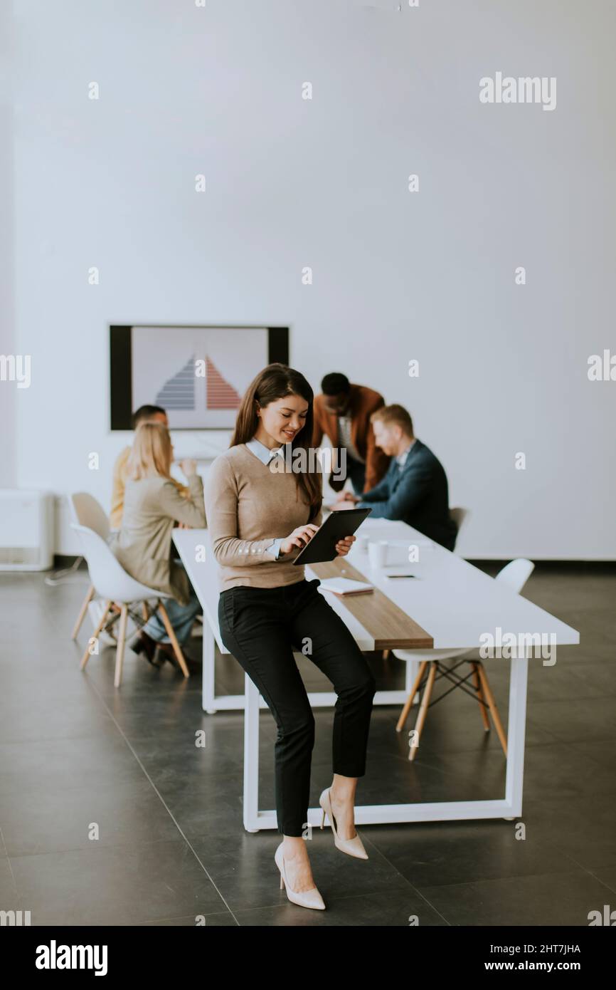 Cute young business woman standing in the office and using digital tablet in front of her team Stock Photo