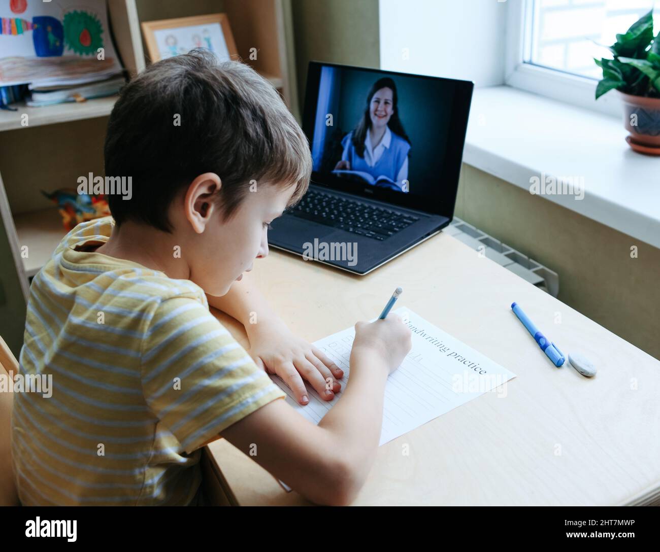8 years old boy sit by desk with laptop and do writing task during