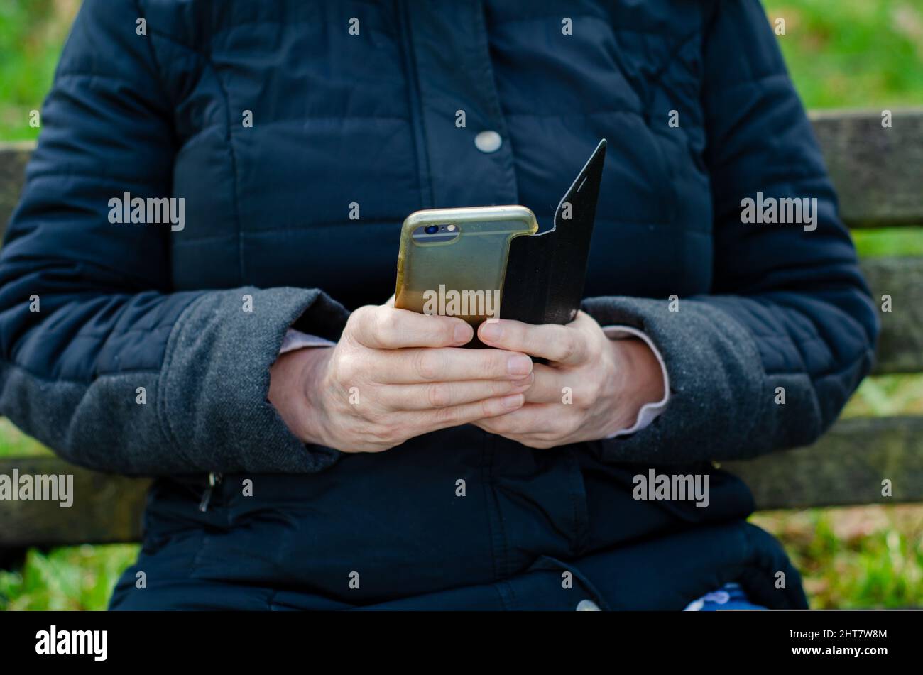 Casually dressed woman sitting on park bench using  mobile cell  phone selective focus Stock Photo