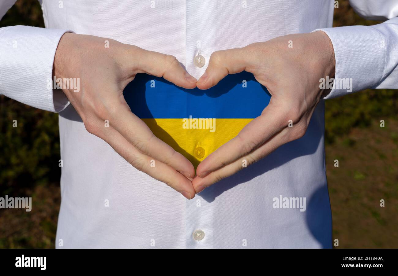 man holidng his hands in heart shaped on white shirt with ukraine flag colors support concept . Stock Photo