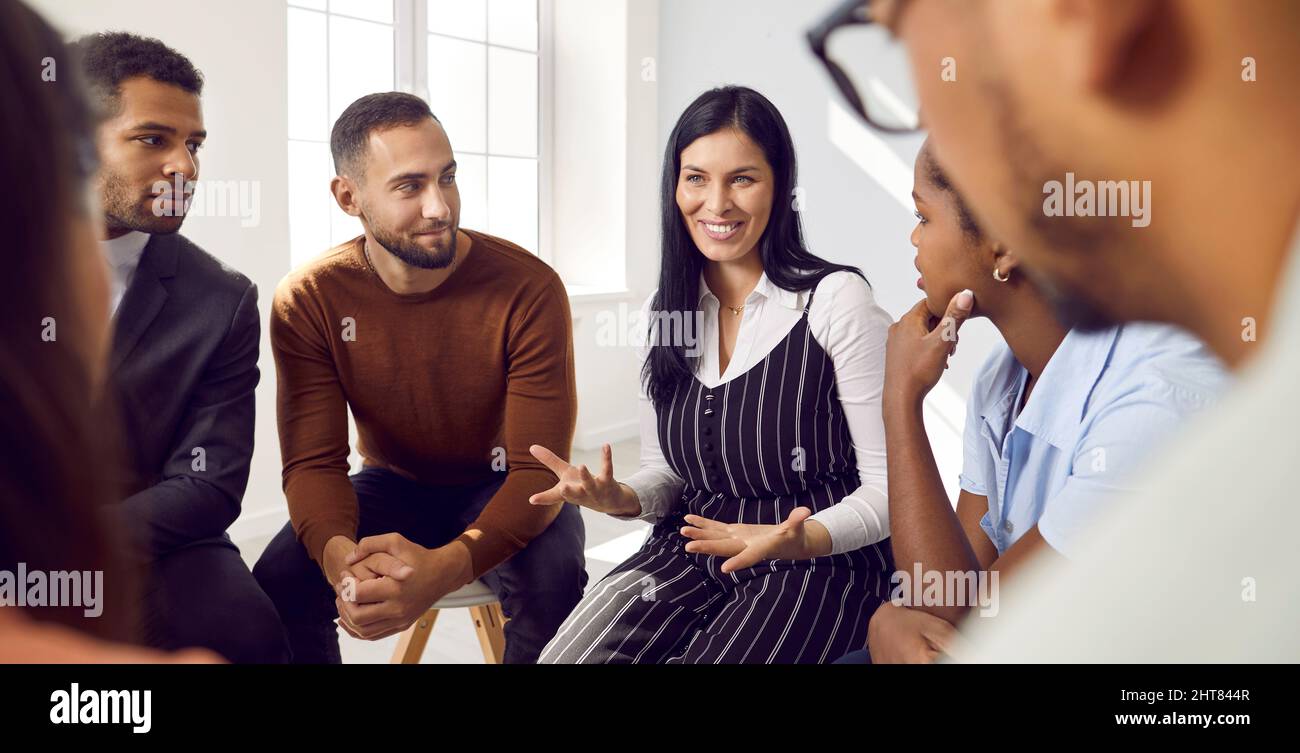 Female coach or team leader tells funny story or joke to diverse team during work meeting. Stock Photo