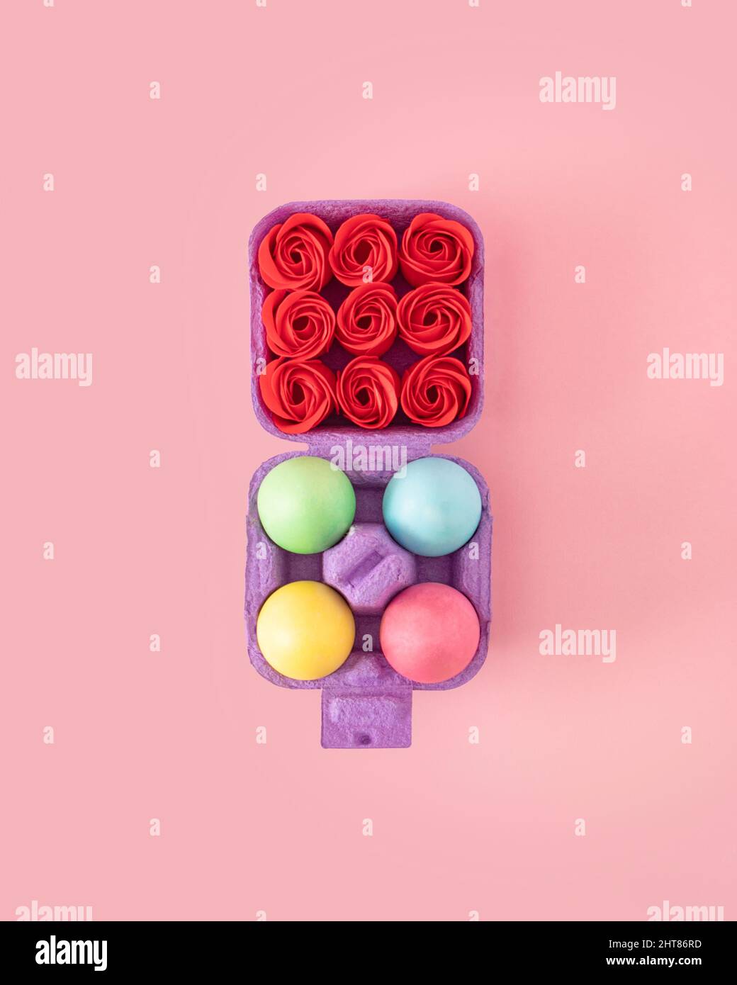 Creative concept of box of colorful Easter eggs on the one side and full of red roses on the other. Pastel color flat lay on spring pink background. Stock Photo