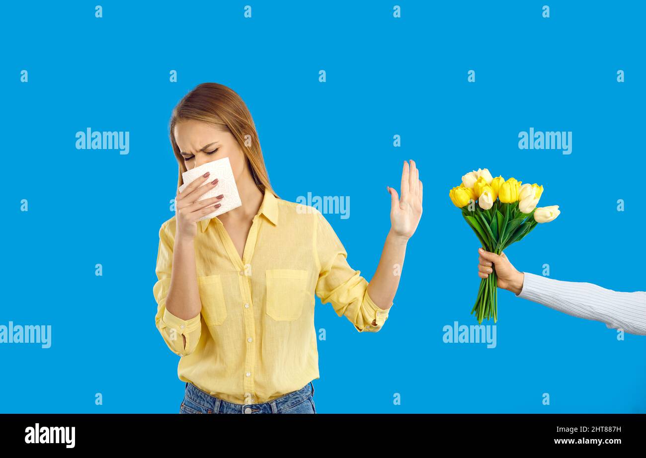 Young woman who has allergic rhinitis sneezes, blows her nose and doesn't accept flowers Stock Photo