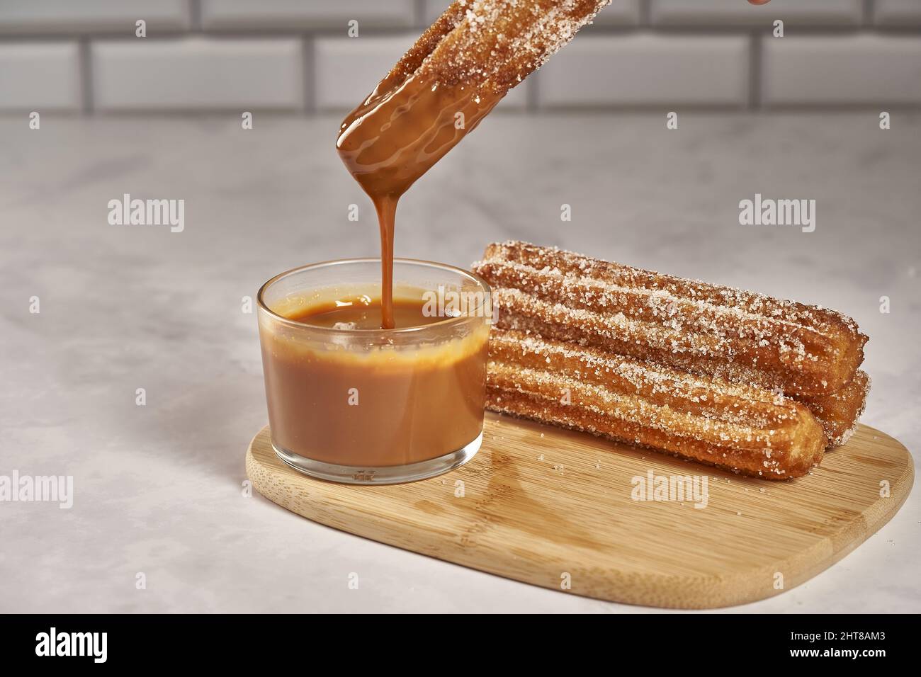 Close up shot of dipping churro in dulce de leche caramel and a wooden