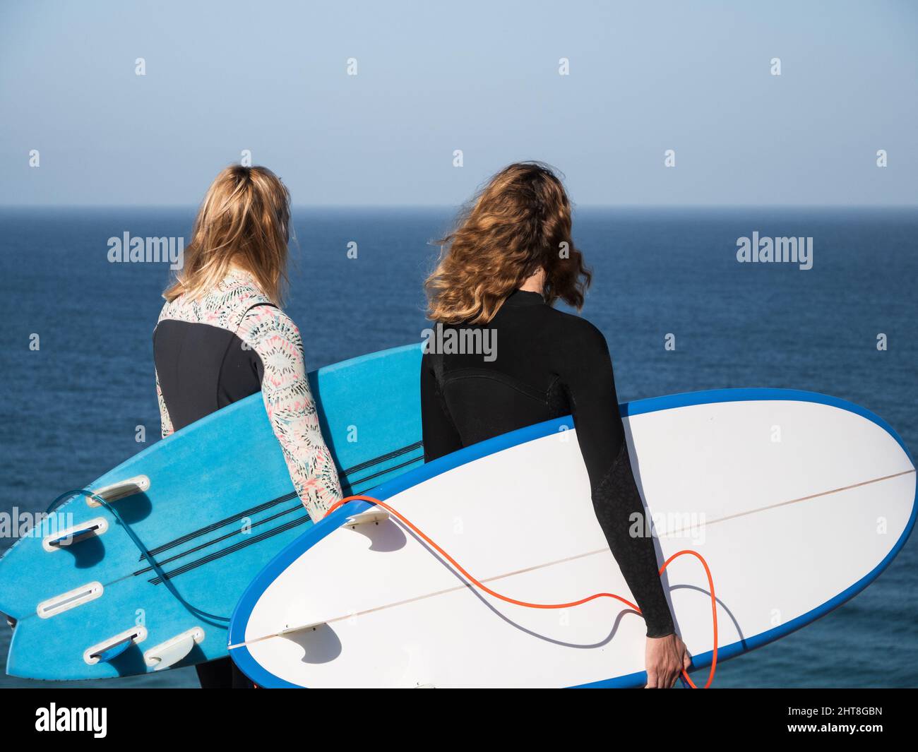 Unrecognizable surfer women watching the ocean holding surfboards Stock Photo