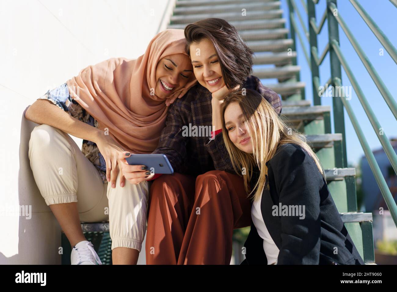 Company of smiling women sitting on stairs and talking Stock Photo