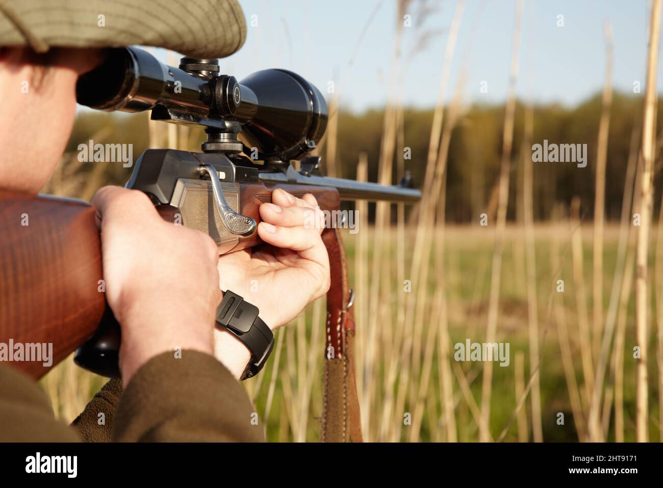 Patience is the secret to a perfect shot. A game hunter looking through the reeds with his sniper rifle. Stock Photo