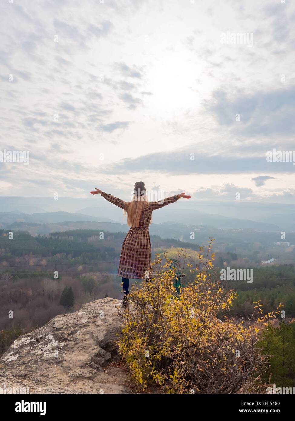 A long-haired woman in a dress stands on the edge of a cliff with her ...
