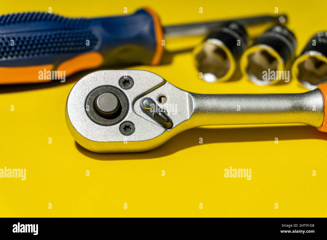 Ratchet head on a yellow table surrounded by other tools mechanics