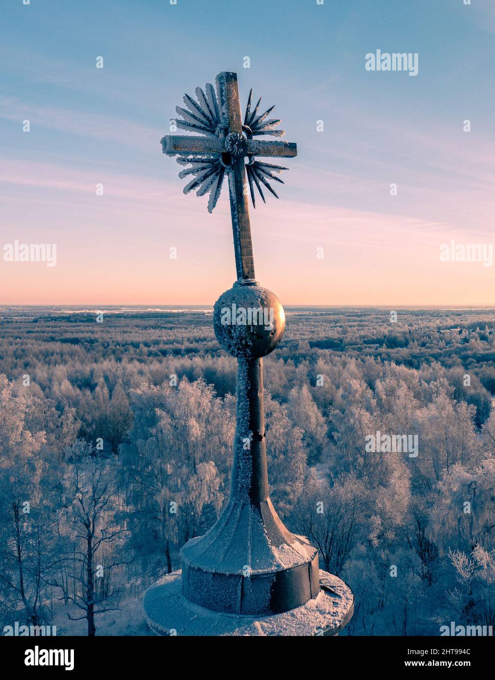 Snowy cross surrounded by trees covered in snow at sunset or sunrise ...