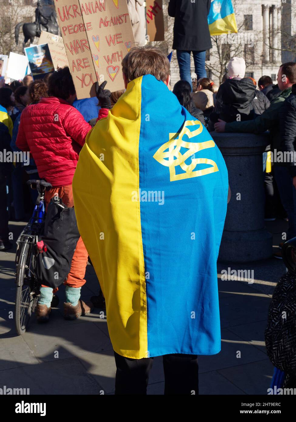 View of a protester draped in the Ukrainian flag in Trafalgar Square London to protest at the Russian invasion of Ukraine Stock Photo