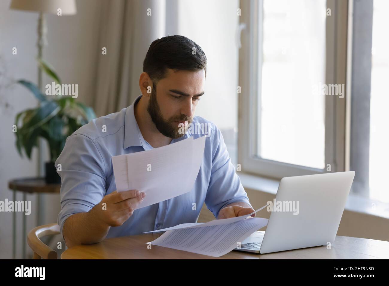 Serious man sit at table with laptop sorting out papers Stock Photo