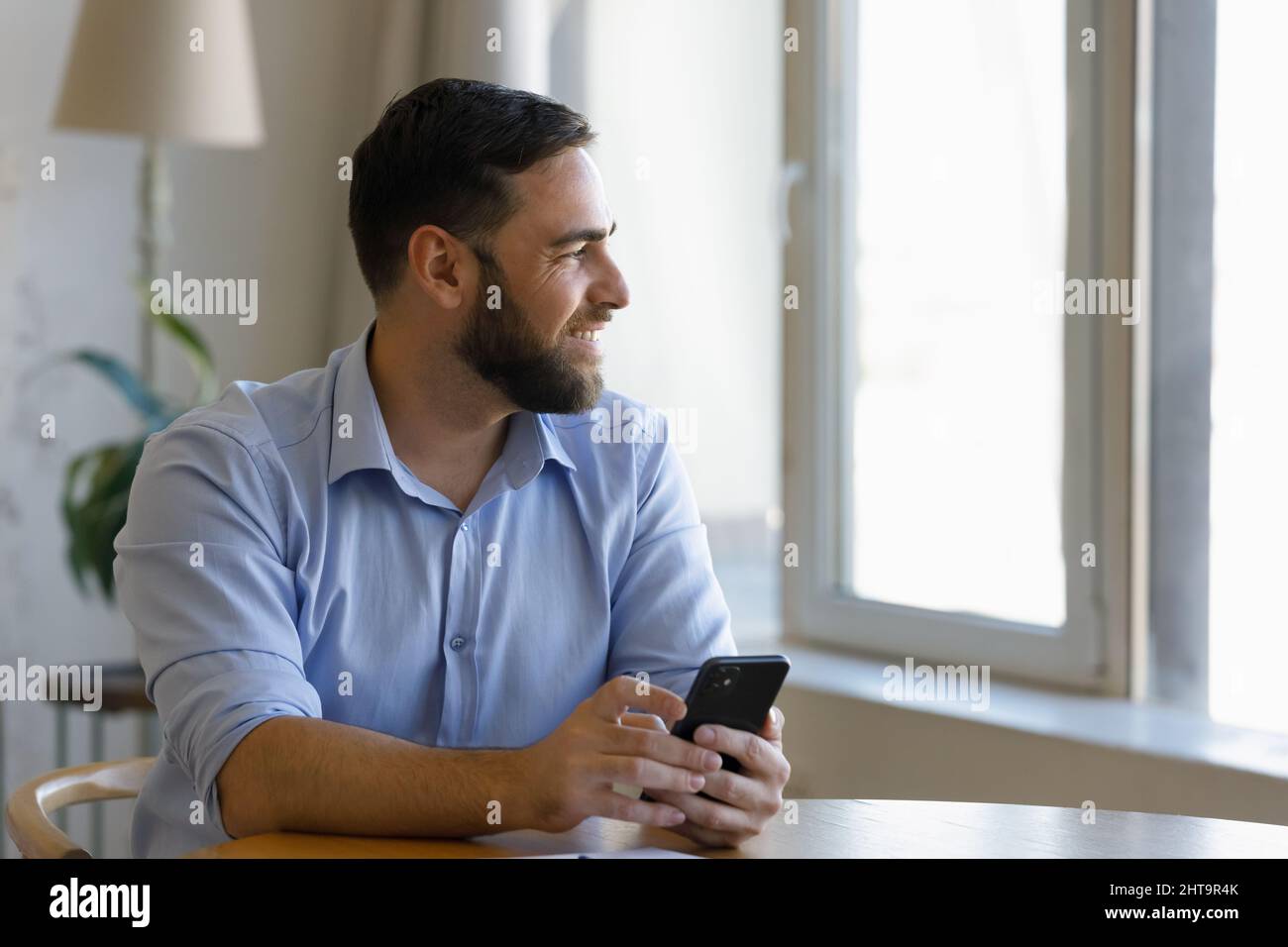 Handsome millennial man sit at table with cellphone in hands Stock Photo