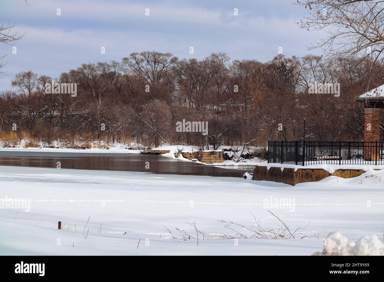 Snowy park on a clear winter day with trees on the background and a small shallow lake in the middle Stock Photo