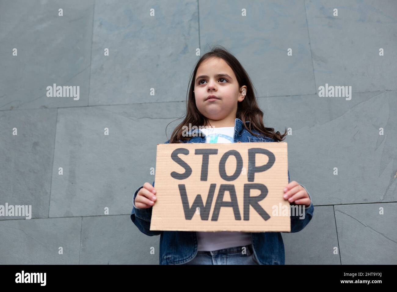 Caucasian little girl demonstrating against war. She is on the street holding a handmade sign. Stock Photo