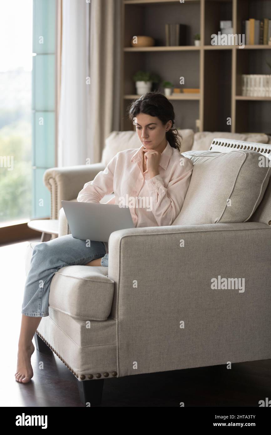 Concentrated young Hispanic woman using computer at home. Stock Photo