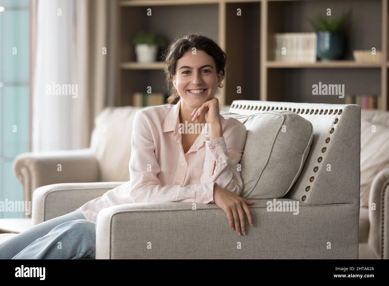 Portrait of smiling young Hispanic woman resting on couch. Stock Photo