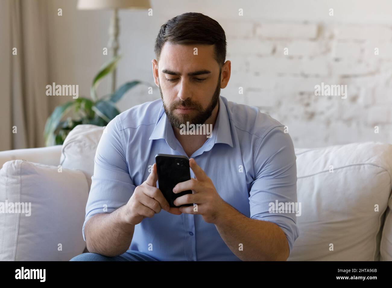 Serious man sit on couch look at cellphone screen Stock Photo