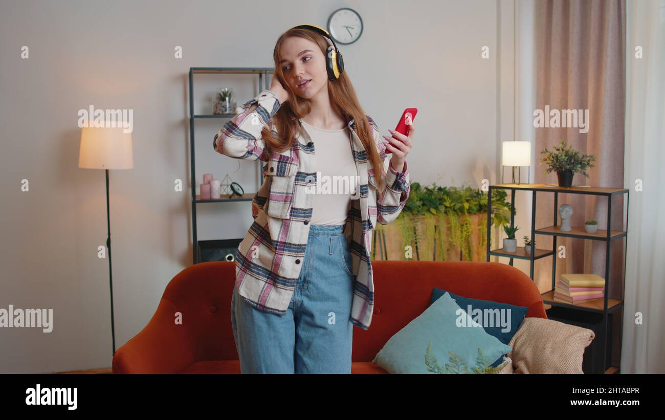 Pretty Caucasian young woman in headphones listening music dancing ...