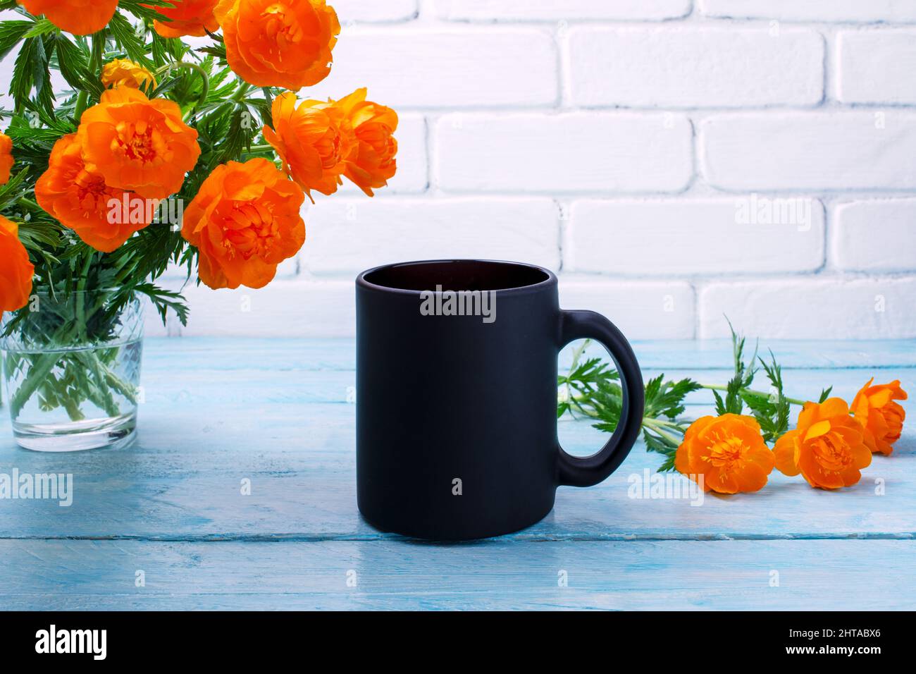 Black coffee mug mockup with globeflowers in the glass vase. Empty mug mock up for brand promotion Stock Photo