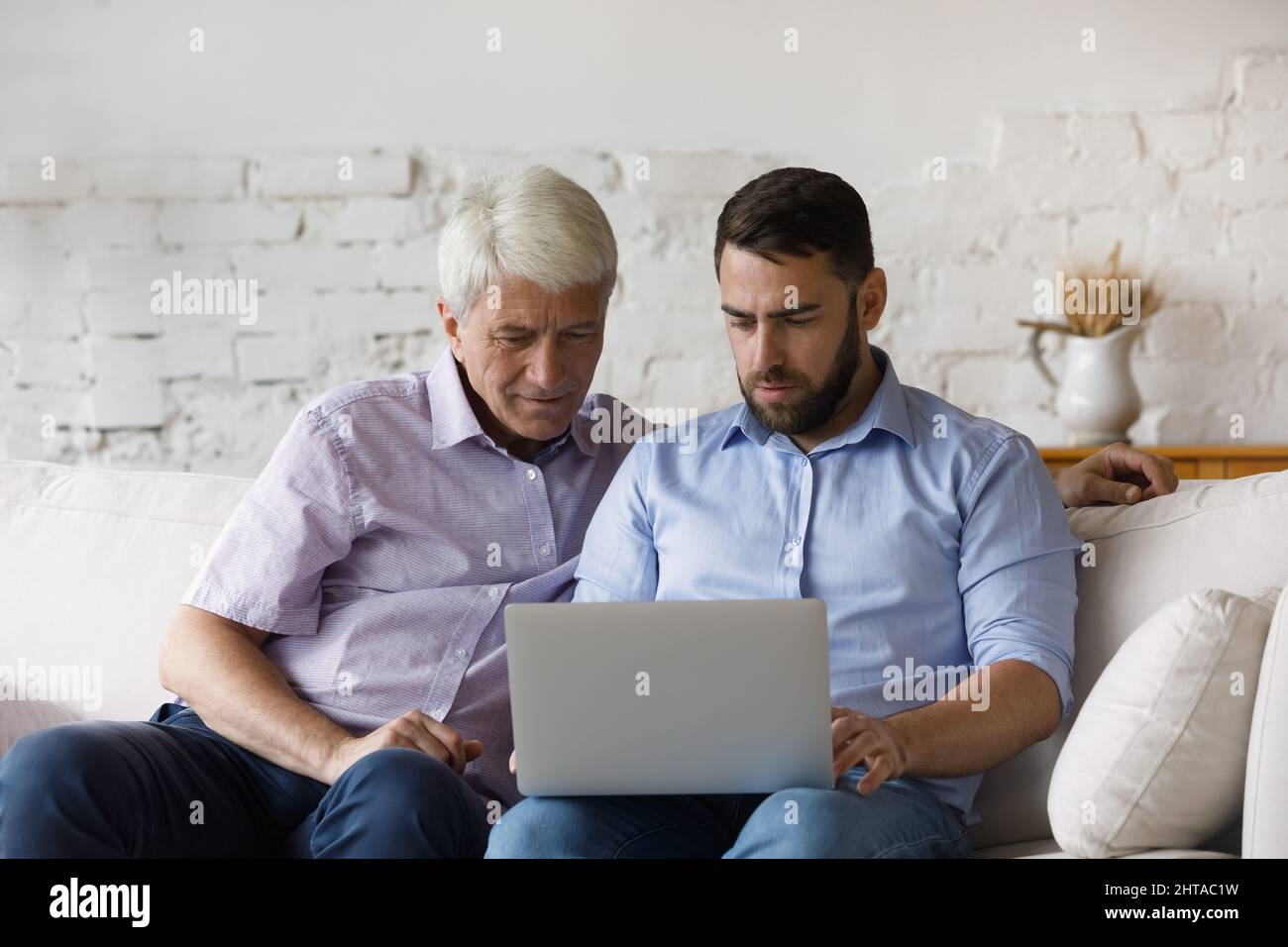 Serious millennial man helps to older father with laptop usage Stock Photo