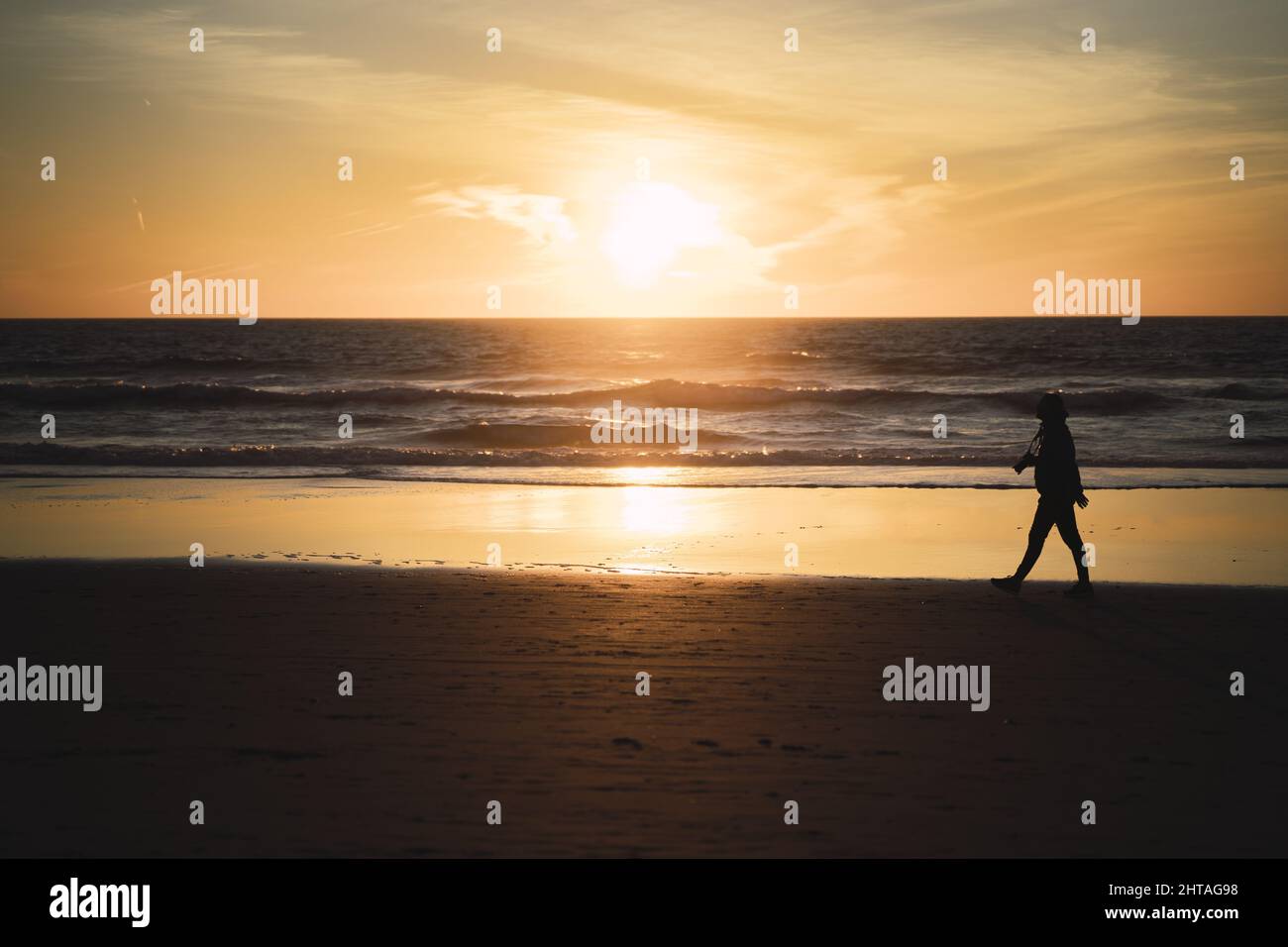 Silhouette of a woman with camera walking on a beach with a magnificent ...