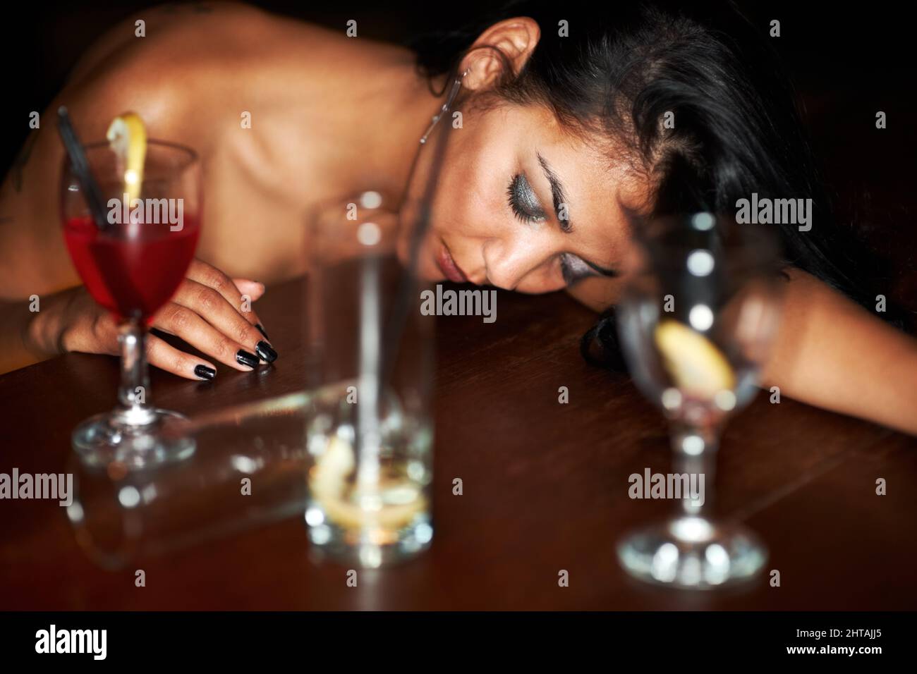 Her night is at its end. A drunk young girl passed out at the bar surrounded by half-finished drinks. Stock Photo