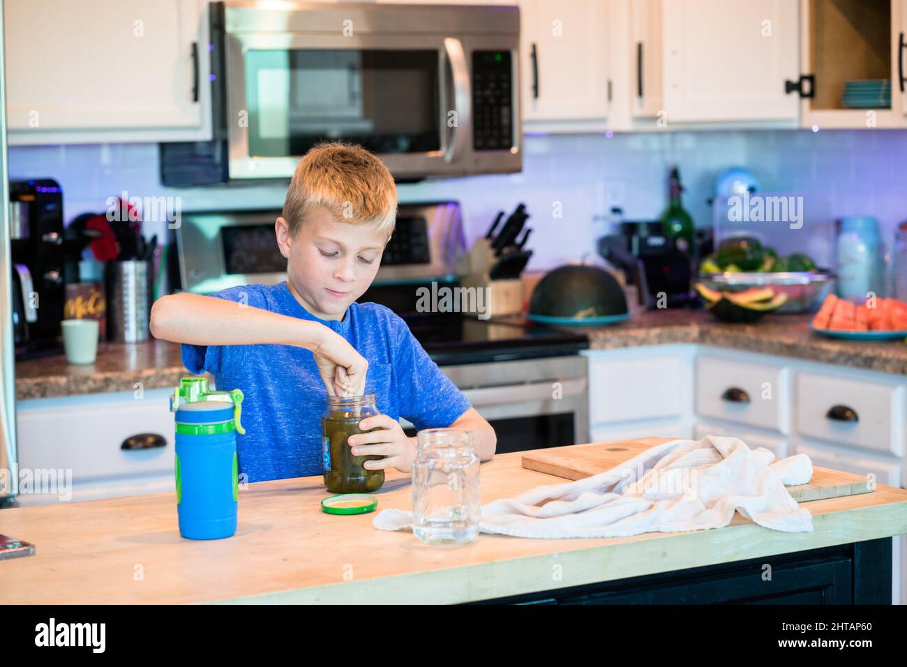 Little boy eating a opening a jar of salted cucumbers Stock Photo