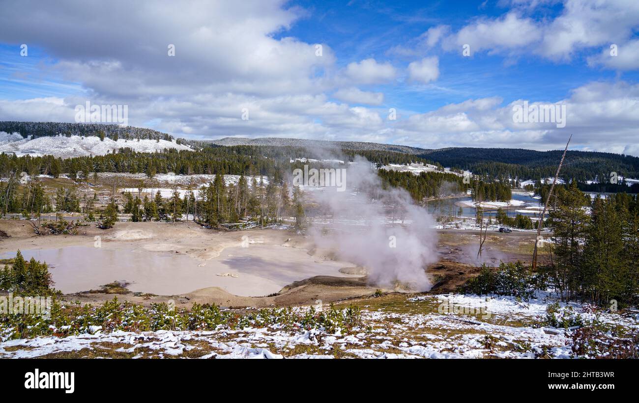 Panoramic Landscape view of trees with steam coming out with range mountains and a blue cloudy sky Stock Photo