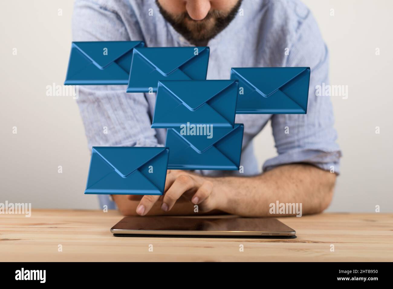 Man scrolling on a tablet with 3D renders of email icons in the air ...