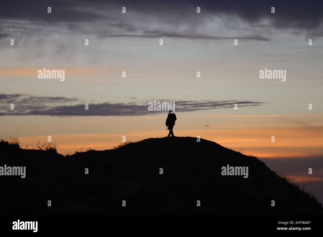 silhouette of a man in a cap sitting on a mountain watching the sunset ...