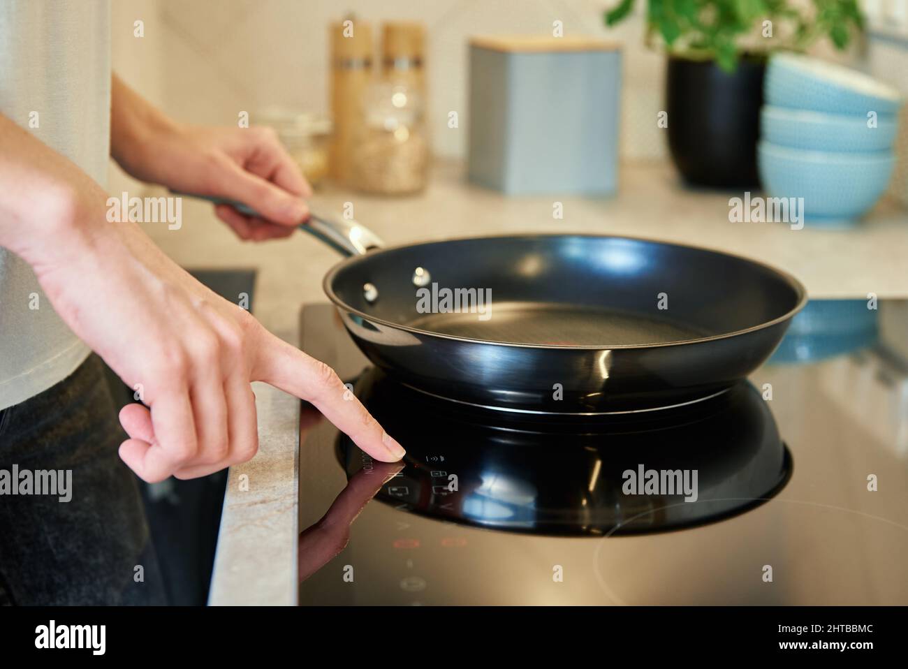 Woman turn on button on induction stove with steel frying pan in the kitchen, Modern kitchen