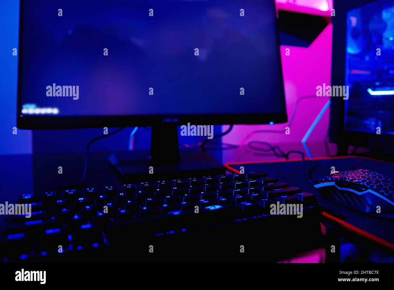PC with rgb keyboard for gaming computer video games with neon colored background, dark room with game workplace without people Stock Photo