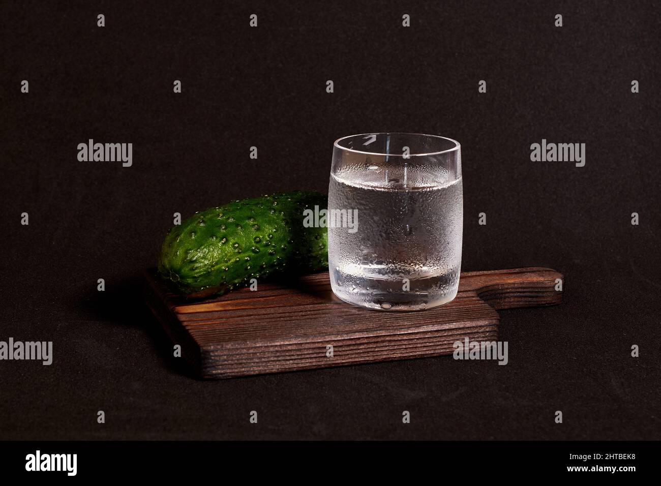 A glass of vodka and a fresh cucumber on a wooden stand  Stock Photo