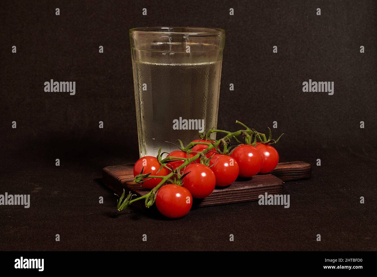 A faceted glass of vodka and a branch of cherry tomatoes on a wooden stand  Stock Photo