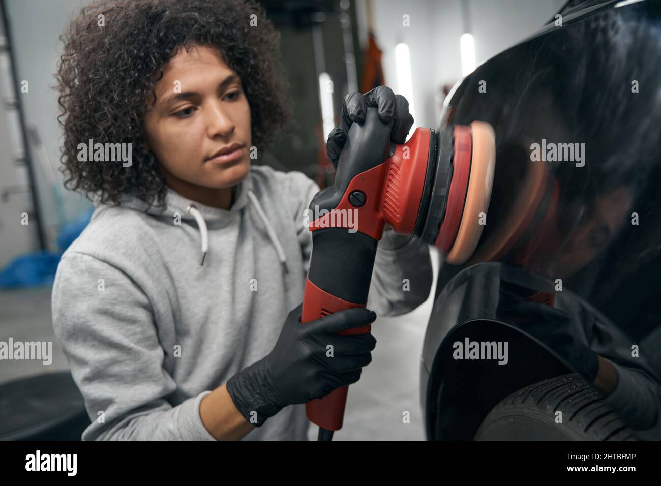 Skilled service station worker polishing automobile with buffer Stock Photo