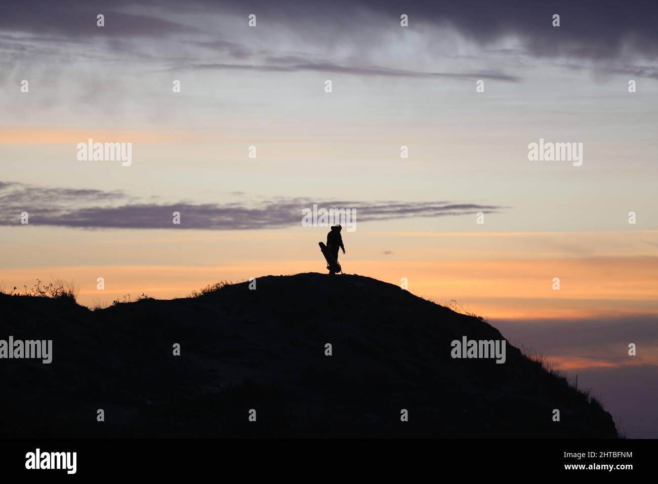 silhouette of a man in a cap sitting on a mountain watching the sunset ...