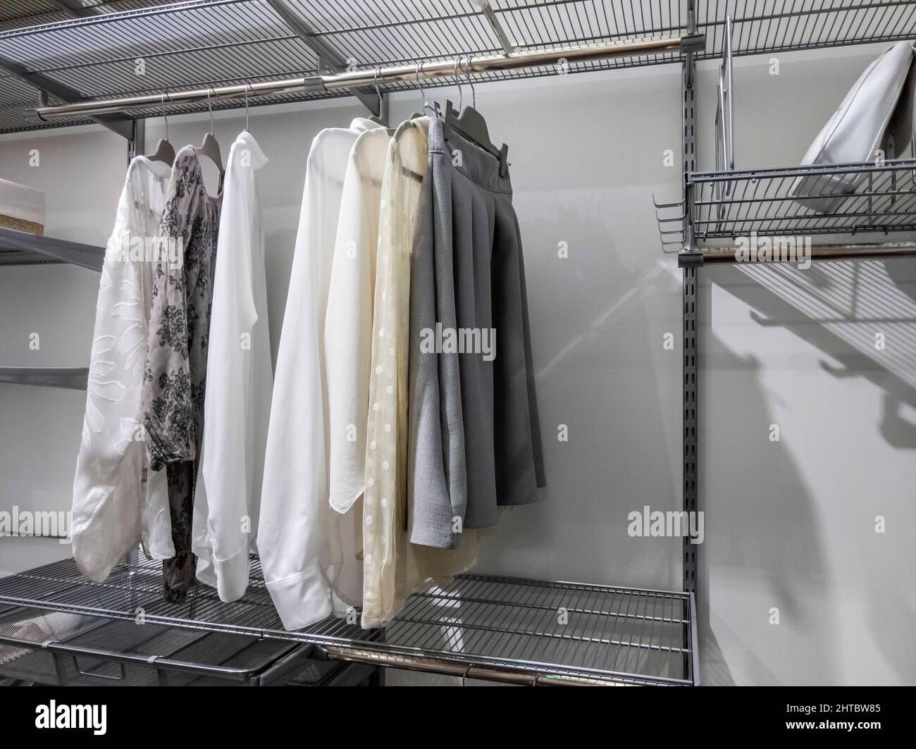 Collection of monotone colors tops and bottoms hanging inside an organized walk in closet with metal wire rack shelving Stock Photo