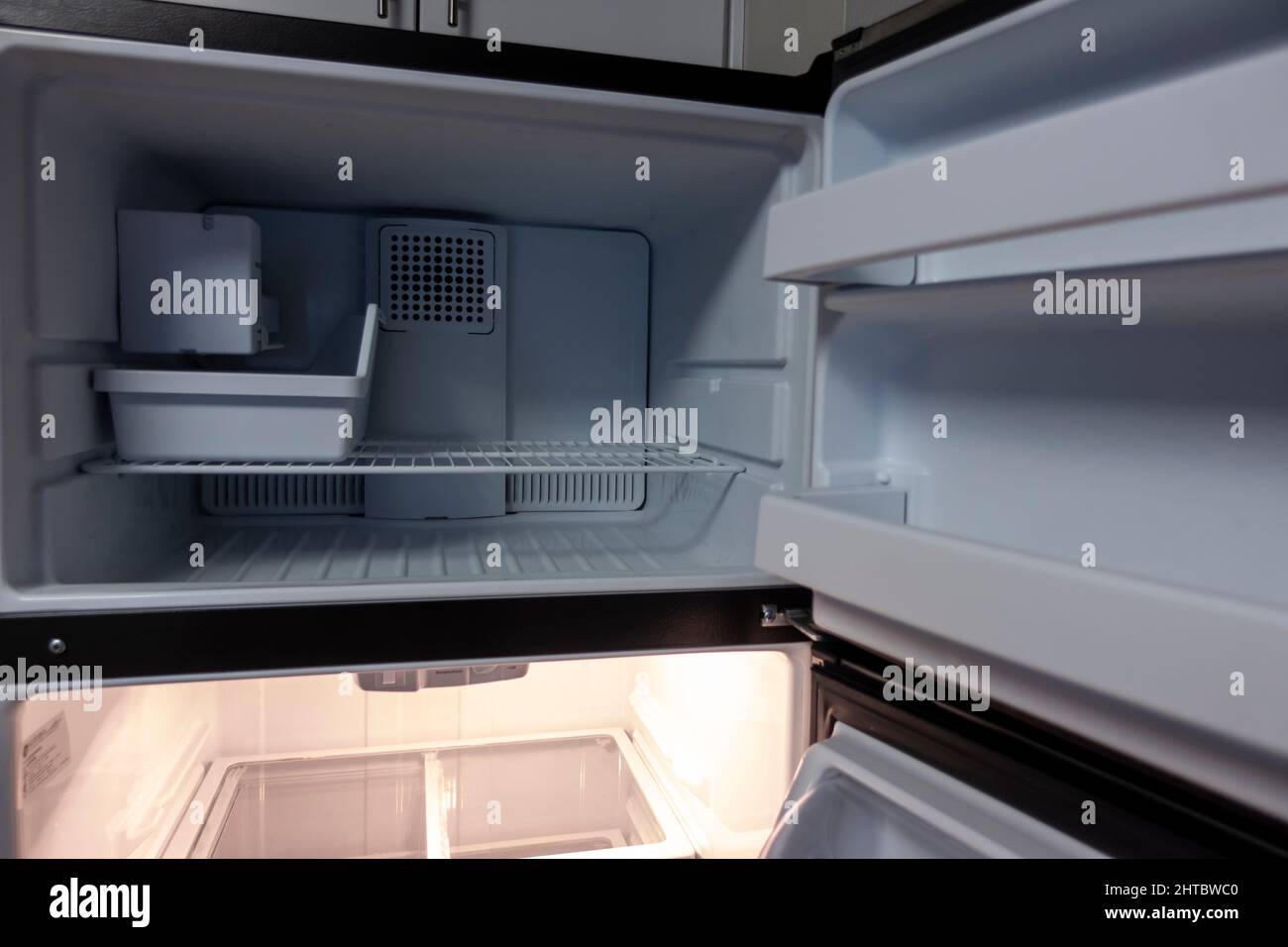 View of a white, empty fridge with the door wide open to see several shelves and drawers devoid of food Stock Photo
