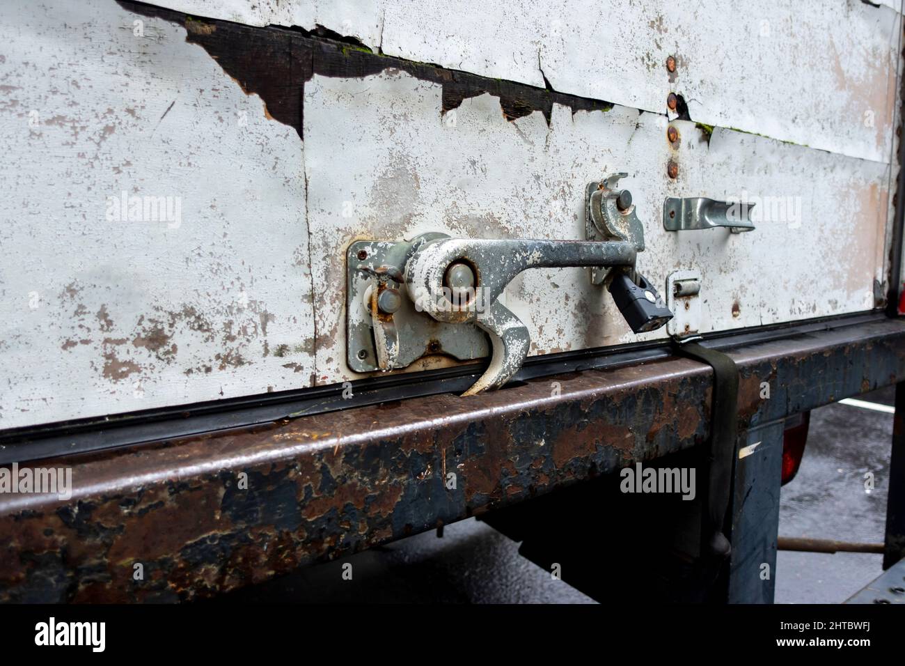 Angled close up view of a rusted metal latch on the back of a white moving truck, with a black step ladder attached Stock Photo