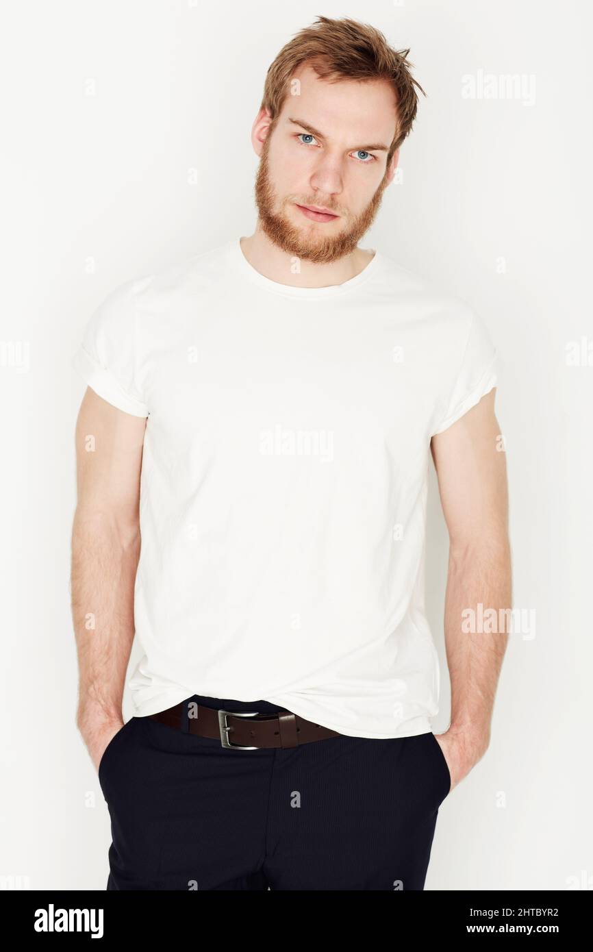 Looking serious. Portrait of a young man standing against a wall with his hands in his pockets. Stock Photo